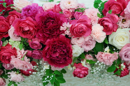 ホテルニューオータニの結婚式の会場装花。濃いピンクの芍薬を主役に、各色のバラ・カーネーション・カスミソウ・グリーンをあしらった横長の高砂装花のクローズアップ