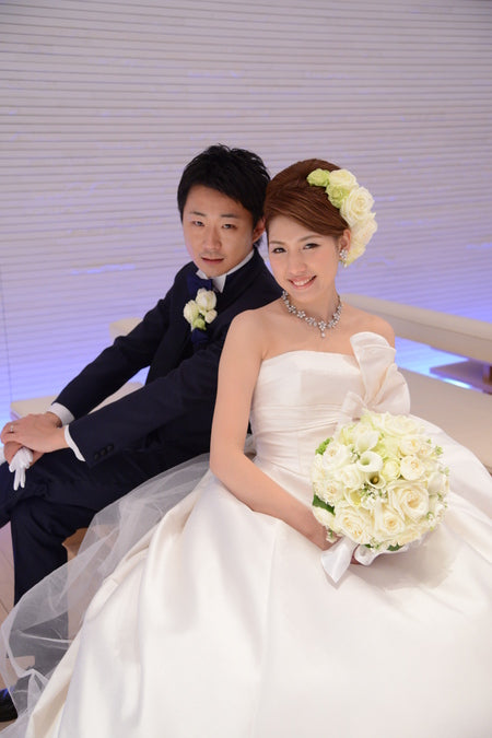 白ドレスの花嫁様とネイビーのタキシードの新郎様。白バラと白いカラーのラウンドブーケと、おそろいの白バラの髪飾り｜コンラッド東京