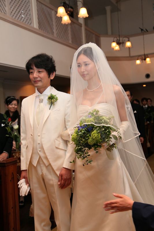 アイボリーのタキシードの新郎様と、白いドレスにベールの花嫁様。花嫁様は緑と青のクラッチブーケを手に｜山手ロイストン教会