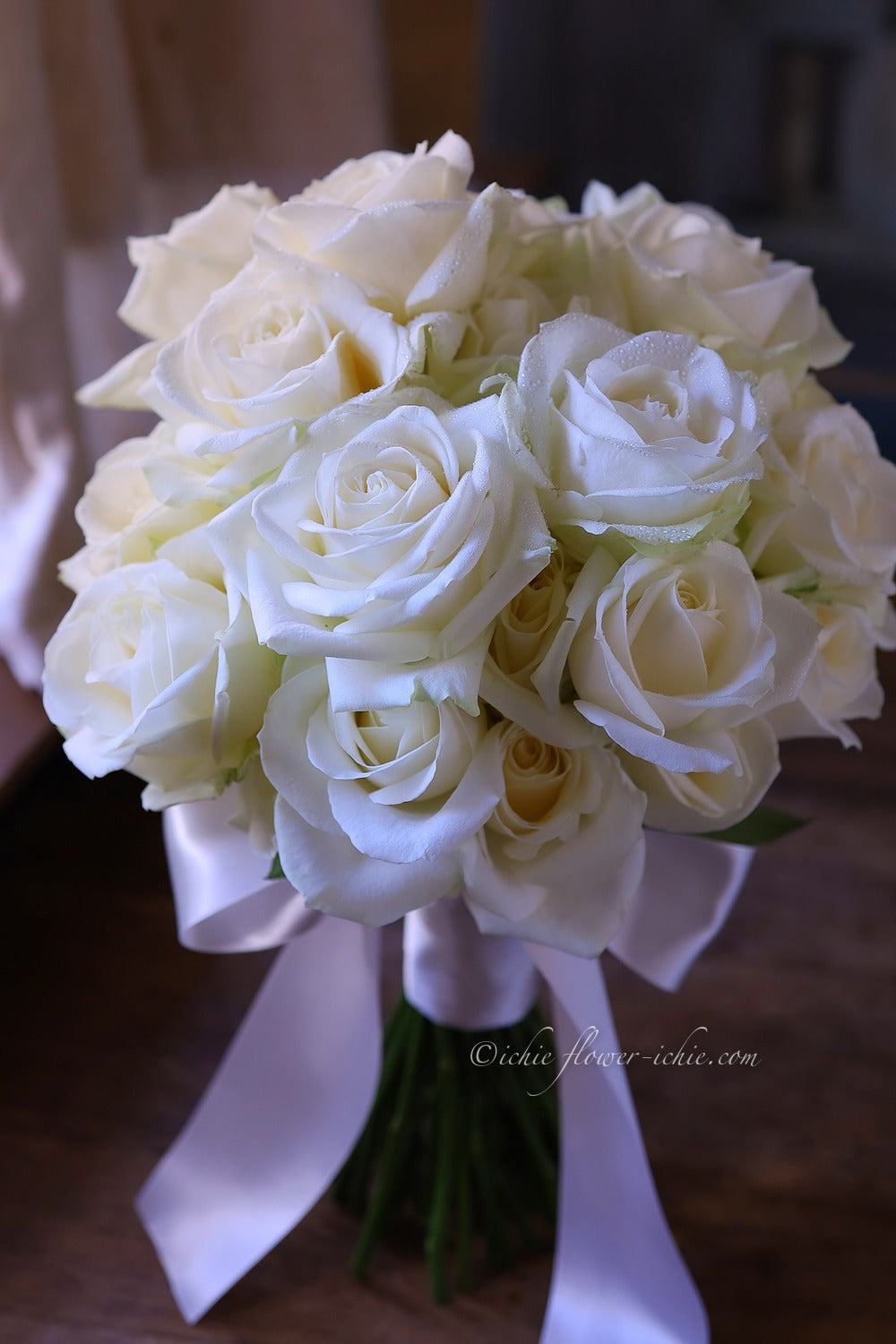 白バラのクラッチブーケの写真。右下にZapfinoの筆記体で©ichie flower-ichie.comの署名が白い文字で蘇っている
