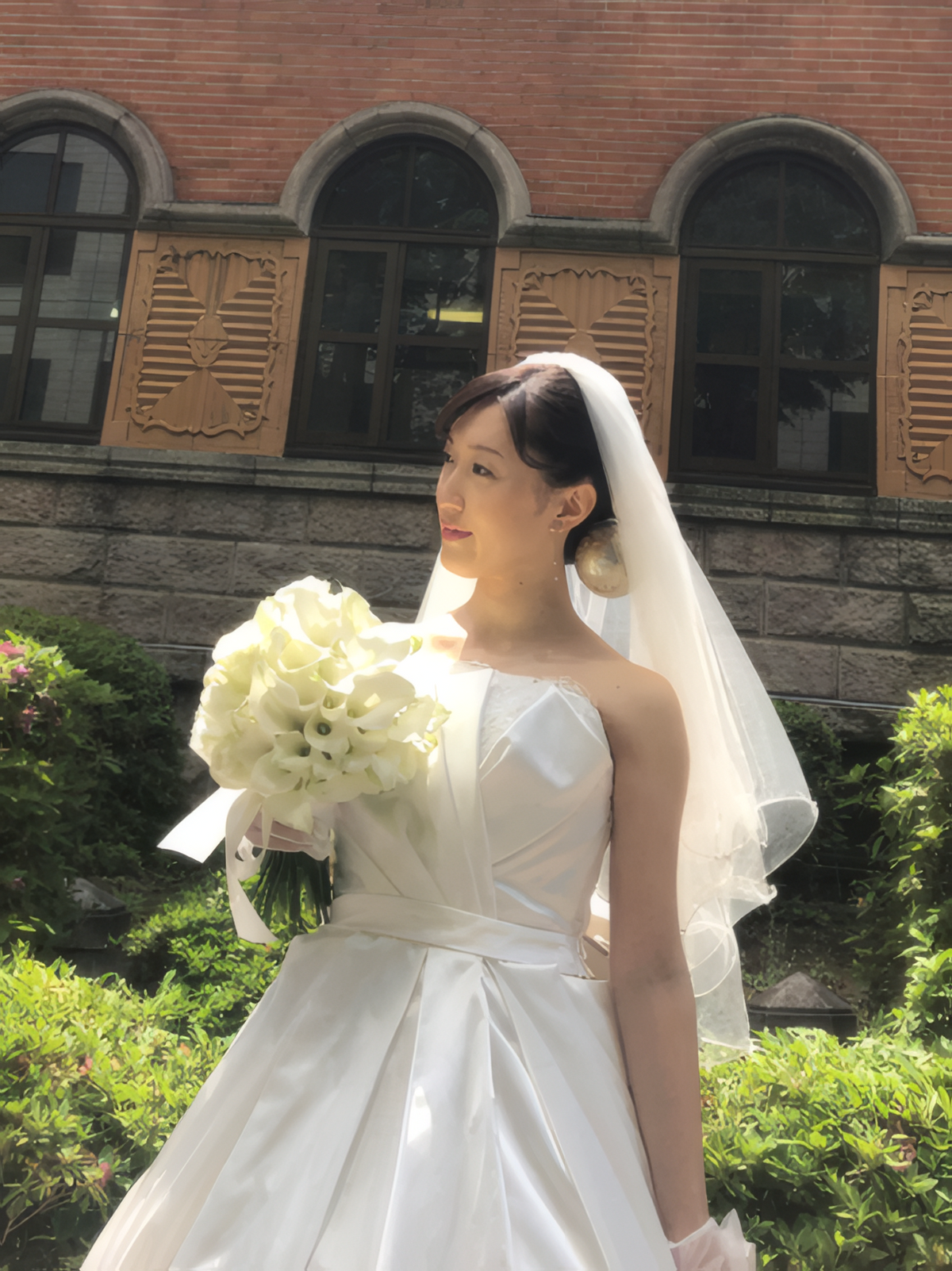 クルトゥルハイム大聖堂のレンガ壁の前で、カラーとバラのクラッチブーケを持つ花嫁様｜東京・白金のウェディングブーケ専門｜一会アトリエ（いちえ）
